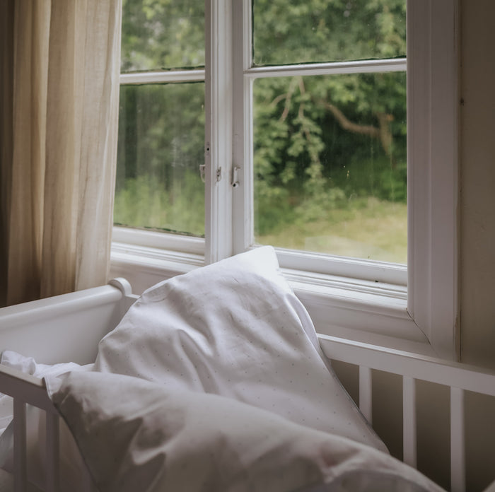 White crib with a white blanket next to a window with a view of greenery