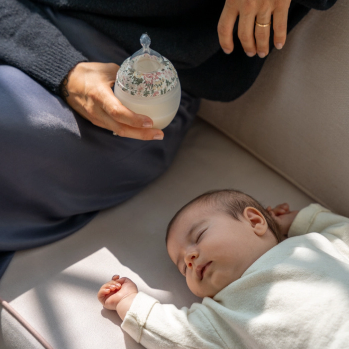 Person holding a baby bottle next to a sleeping baby