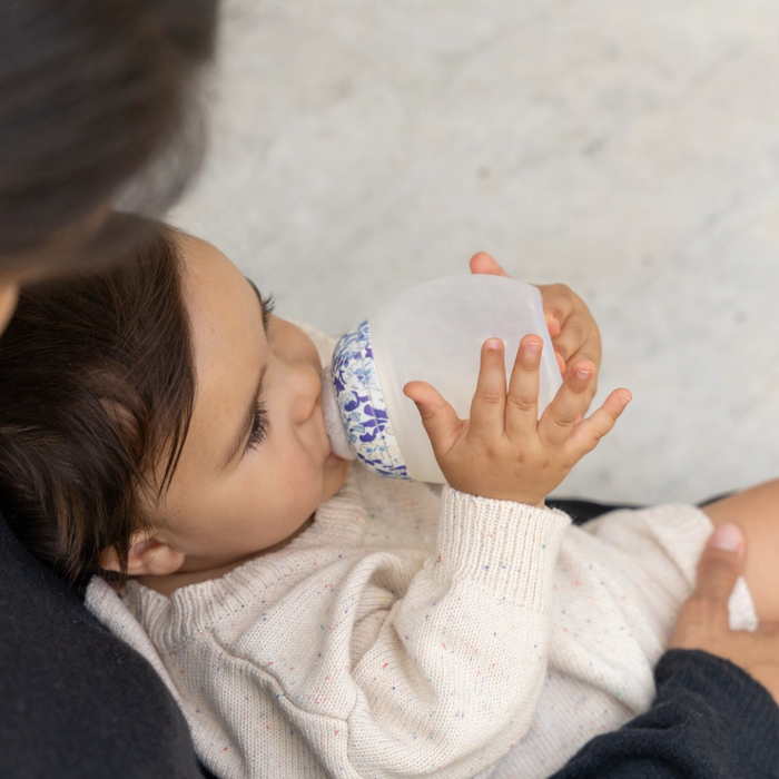 Baby holding a baby bottle with blue patterns, lying on a soft surface.