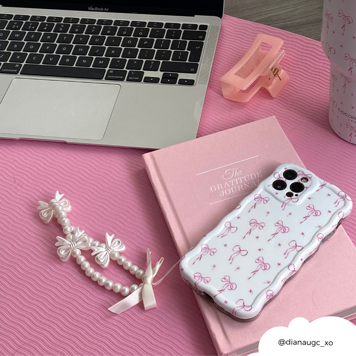 Smartphone with a pink bow case and pastel beaded phone strap on a pink desk.
