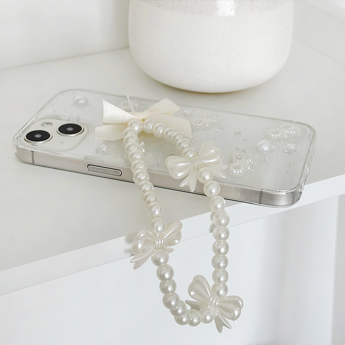 White phone in a clear case with a pastel beaded Coconut Lane phone strap on a white shelf.