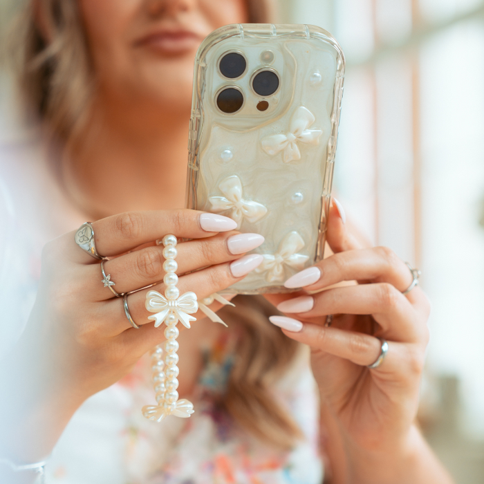 Hand with manicured nails holding a phone with Coconut Lane’s pink and white beaded phone strap attached.