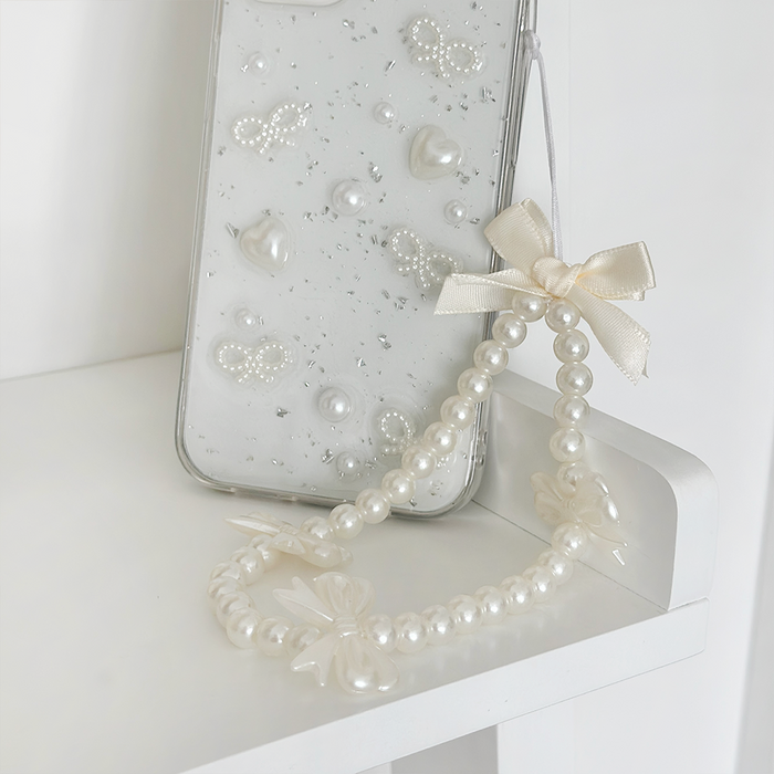 Phone in pearl and bow case next to pastel beaded phone strap on a white shelf.