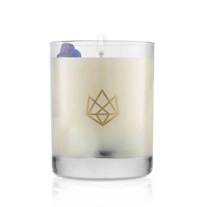 Lit white candle in a clear glass container with a subtle gold geometric logo, featuring small decorative blue stones, Calm Glass Candle | Aluminate Life.