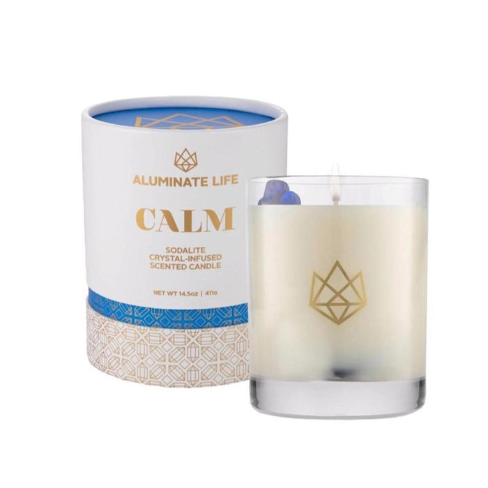 Calm Glass Candle | Aluminate Life with a lit wick, featuring crystal accents inside a clear glass holder next to its elegant white and blue packaging designed for relaxation and wellness.