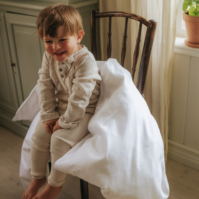 Child sitting on a chair with a white blanket, smiling in a home setting.