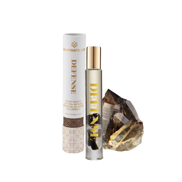 Defense RollerBall | Aluminate Life skincare rollerball with smoky quartz crystal beside decorative packaging and a natural stone for wellness and recovery.