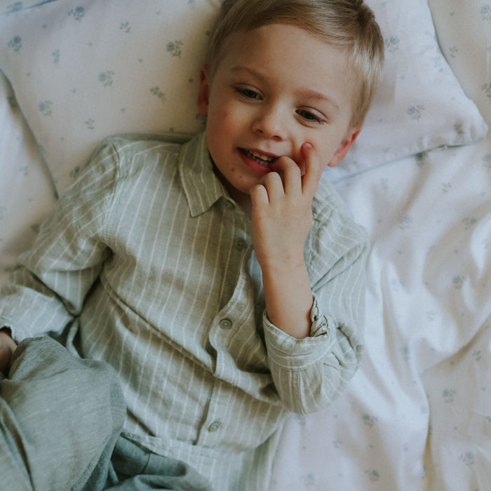 Child in a green shirt lying on a floral-patterned bed