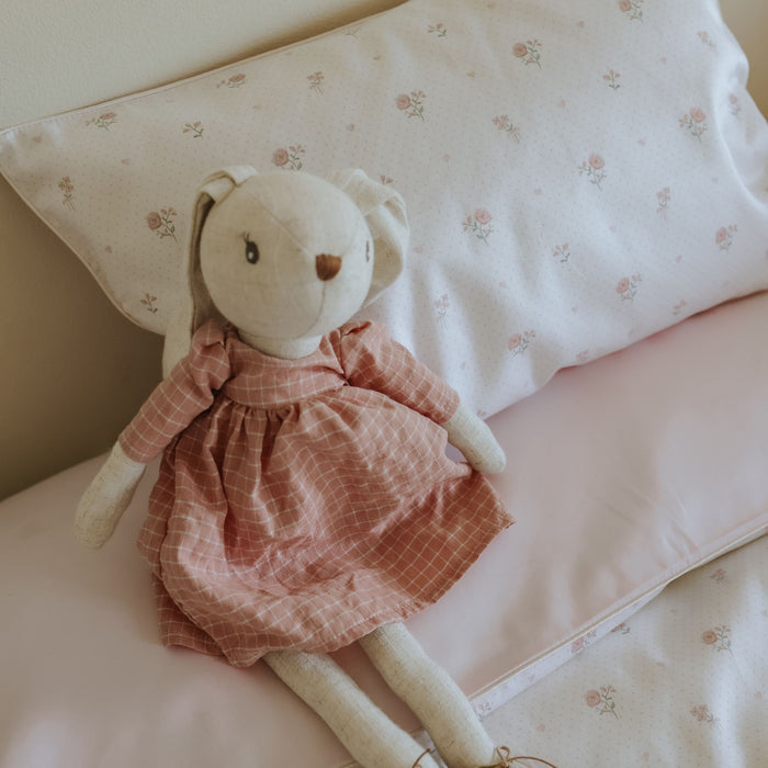 Stuffed animal bunny toy with a pink dress on a floral-patterned pillow
