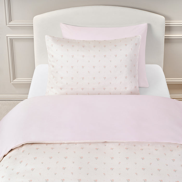 Twin bedding set in the pattern Ditsy Floral in Pink on a bed with a white headboard.