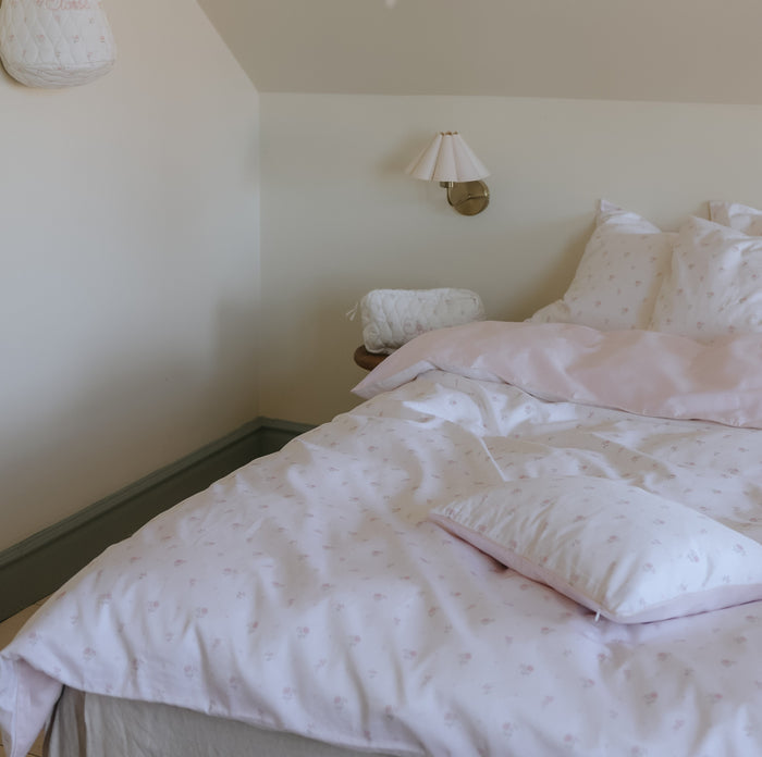Bedroom with a bed featuring pink bedding and pillows, wall lamp, and light-colored walls.