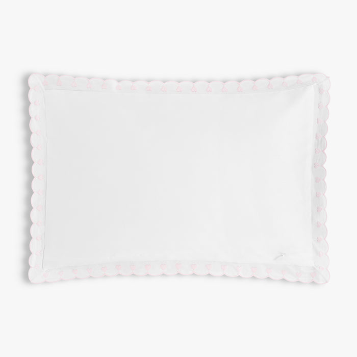White pillow with scalloped pink embroidered edge on a white background