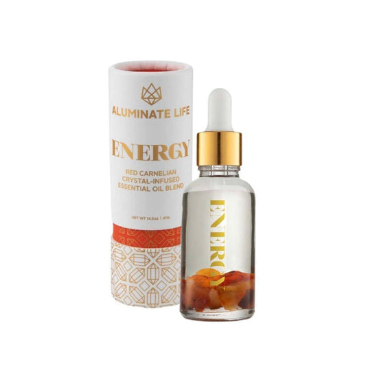 Clear glass dropper bottle with golden cap containing a crystal-infused oil blend next to a white and gold decorative cylindrical box labeled Energy Essential Oil Vial | Aluminate Life.