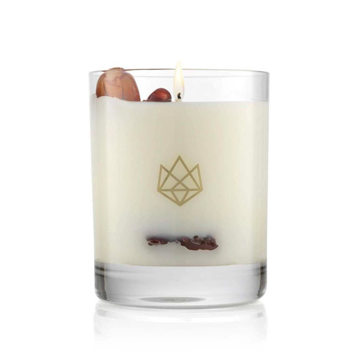 Lit white candle in clear glass with natural stones embedded inside, featuring a subtle gold geometric logo, named Energy Glass Candle | Aluminate Life.