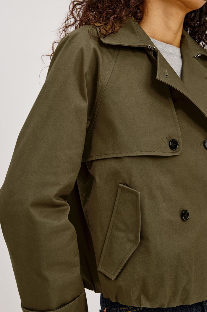 Jett Cropped Trench Jacket in Cotton Garbardine With Double-Breasted Design, Structured Collar, Pockets, and Long Cuffed Sleeves in Olive Colorway - Upper Body Close Up View Featured on Model