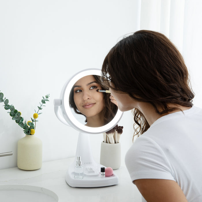Zadro MAX110 705004420549 environment photo front view user applying makeup on bathroom countertop, max bright lighted makeup mirror with magnification & storage tray in front of a real life setting