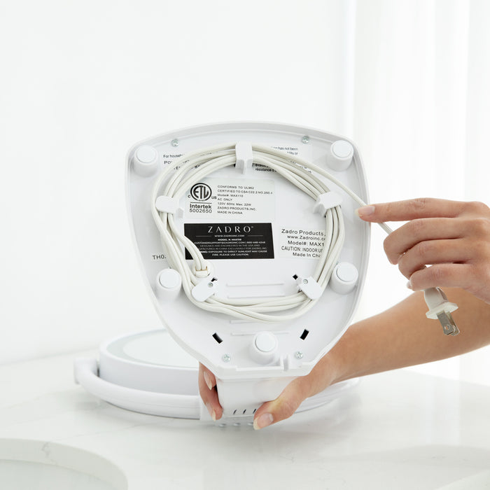 Zadro MAX110 705004420549 environment photo user wrapping cord in storage underneath the base , max bright lighted makeup mirror with magnification & storage tray in front of a real life setting