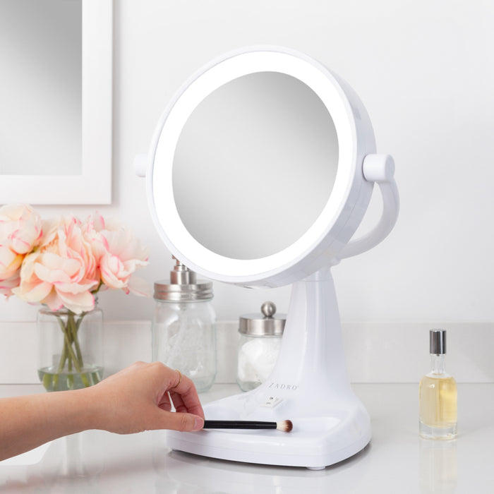 Zadro MAX110 705004420549 environment photo side view user placing makeup brush in storage tray, max bright lighted makeup mirror with magnification & storage tray in front of a real life setting