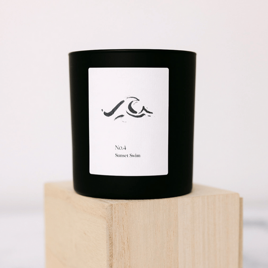 No. 4 Sunset Swim (Amalfi Coast) Candle | Lucky Owl in a minimalist black glass container with white label featuring abstract wave design, placed on a light wooden block.