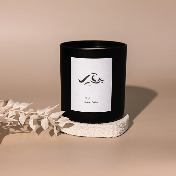 No. 4 Sunset Swim (Amalfi Coast) Candle | Lucky Owl in a sleek black container with minimalist label, placed on a textured white platform with soft neutral background.