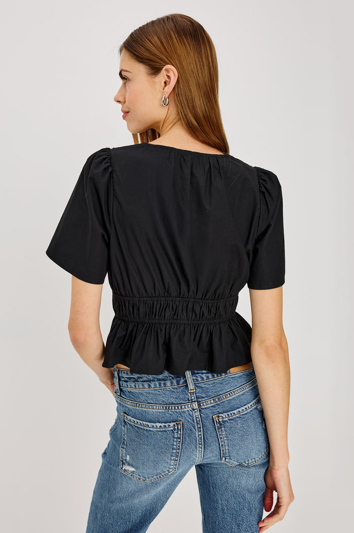 Orla Shirt in Cotton Poplin With Short Puff Sleeves, Deep V-Neckline, Shirred Shoulders, Elastic Waist and Underbust, and Peplum Hem in Black Colorway - Upper Body Back View Featured on Model