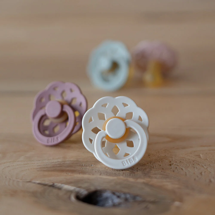 Four pacifiers in different colors on a wooden surface