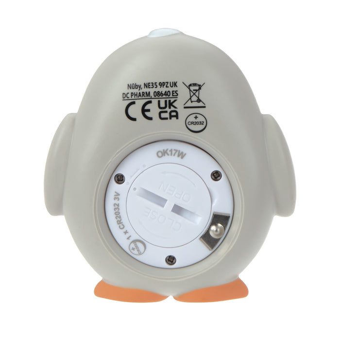 The Nuby Penguin Bath & Room Thermometer is gray, penguin-shaped, shown from the back with a battery compartment marked open and close, orange feet, certification symbols, and product info printed on the surface.