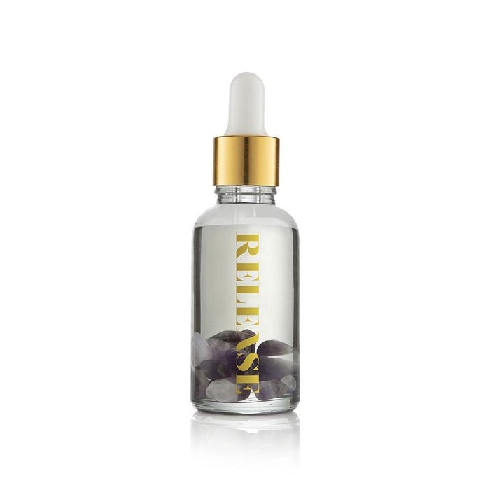 Clear glass dropper bottle with gold cap containing black stones inside labeled Release Essential Oil Vial | Aluminate Life for wellness and body care use