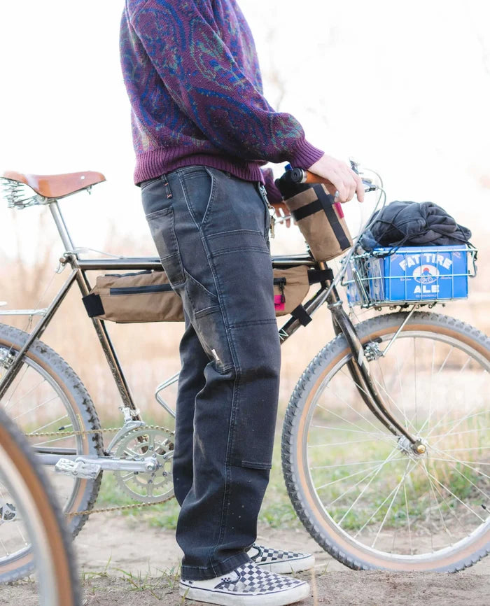 Black RIPTON twill utility pants with double-knee panels and carpenter pockets, worn by a cyclist standing next to a bike.