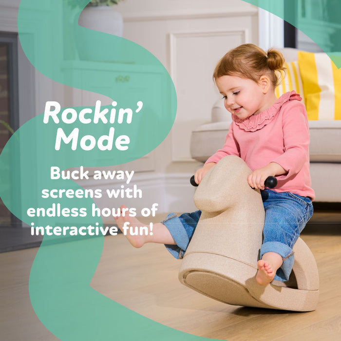 A young child in a pink top and jeans smiles while riding the Rock 'N Ride | Beige 3-in-1 toy indoors. Text on the image reads, “Rockin’ Mode. Buck away screens with endless hours of interactive fun!”.