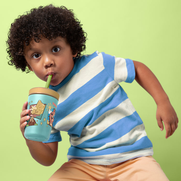 A young child with curly hair in a blue and white striped shirt sips from the Nuby Thirsty Kids Flexstraw Stainless Steel Cup | Dinosaurs, featuring cartoon dinosaurs and a green straw, against a pastel green background.