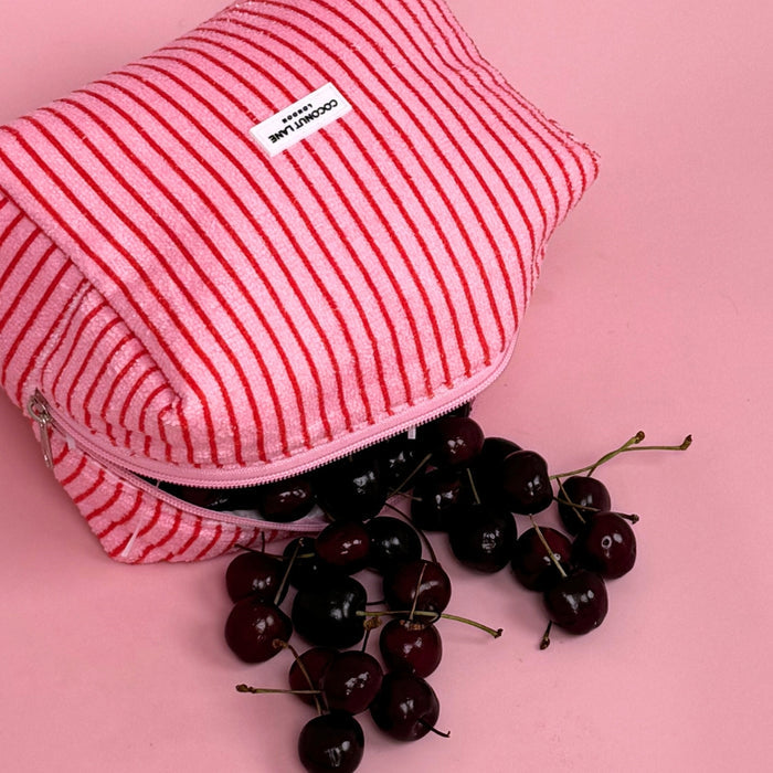 Coconut Lane Cherry Stripes towel makeup bag on a pink background with cherries spilling from the open bag.