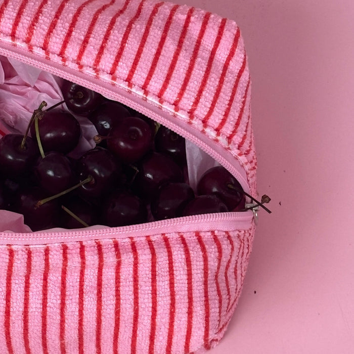 Coconut Lane Towel Makeup Bag in cherry stripe pattern, partially open with cherries visible, on a pink background.
