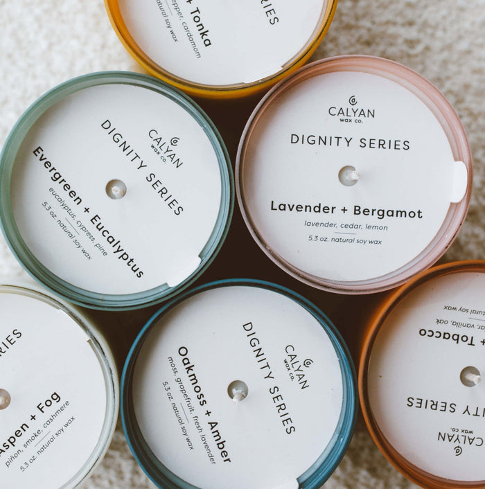 Vetiver + Tonka Dignity Series Glass Jar Soy Candle | Calyan Wax Co. - 5.3 oz displayed among other scented candles arranged in a circle on a soft surface.